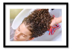 Professional hairstylist washes client’s hair with conditioner shampoo for washing after curling hair. Close up of curlers in hair. Creating hairstyles by a hairdresser in the salon. Shallow depth