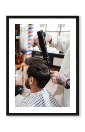 tattooed hairdresser in wristwatch drying hair of client in barbershop.