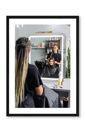 hairstylist spraying hair of happy woman, hairdresser with braids holding spray bottle near female client with short brunette hair in salon, hair extension, hair treatment, hairdo, blurred foreground
