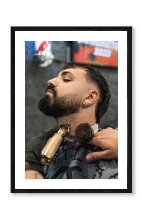 Vertical image of a barbershop customer grooming his beard with a hair clipper in the barber shop.