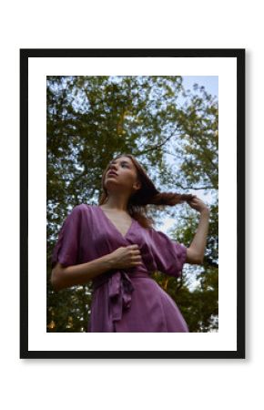 a happy woman straightens her hair while walking in the park in a summer dress