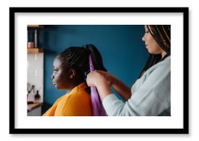 Close-up of hairdresser braiding hair to a young African woman in salon