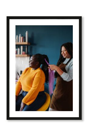 Confident African American hairdresser braiding hair to a smiling female customer in salon