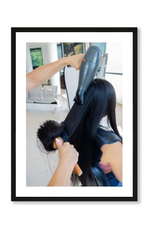Secado de cabello profesional a chica joven clienta con pelo negro, largo y liso. Manos de peluquera con secador de pelo y cepillo moldeador en Salón de Belleza. 