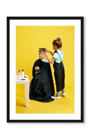 little girl plays the role of hairdresser brushing hair of little boy who sitting on chair against vibrant yellow background. Concept of children dreams, future career, occupation, games, fantasy. Ad