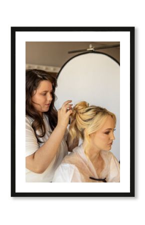 Young female stylist styles the hair of blonde woman. Styling hairstyles for wedding or event. Vertical