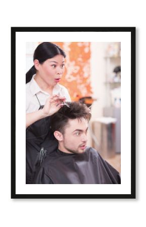 Serious looking handsome man looking at mirror. Beautiful young hairdresser working in hairdressing salon and making haircut for handsome man.