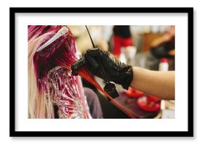 A hair colourist applying pink hair colour to a client's long blonde hair.