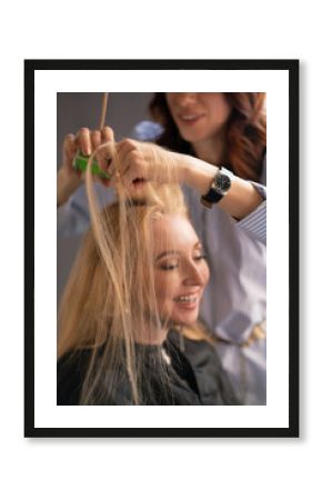 beautiful adult blonde client sits in a chair while a hairdresser master in the salon does her hair with a corrugation and a Perm