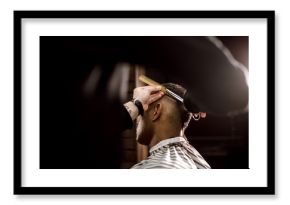 The barber scissors hair on the sides for a stylish black-haired man in the barbershop. Men's fashion and style
