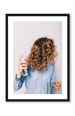 Young woman with long curly hair applying cosmetic care product