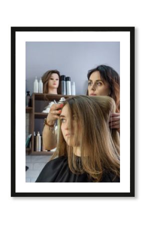 Professional hairdresser using hairspray on long brown hair. Process of hair styling in beauty salon
