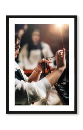 Woman getting a new haircut. Female hairstylist cutting her long black hair with scissors in hair salon