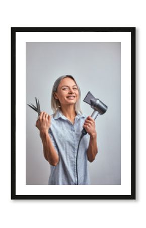 Attractive woman blonde hairdresser with professional tool posing on camera, gray background. Copy space, advertising banner, beauty concept.
