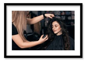 Female hairdresser makes hairstyle on young woman with brunette hair in salon.