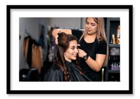 Female hairdresser makes hairstyle on young woman with brunette hair in salon.