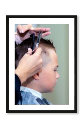 Serious school boy ready getting trendy haircut from expirienced barber at fashionable hairdressing salon.