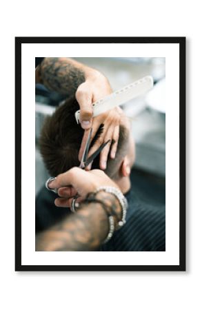 Tattooed barber holding comb while cutting hair of client