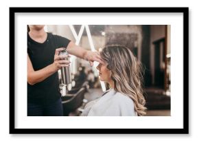 Beautiful young woman with long curly hair in hair salon. Professional hairdresser styling with hairspray.