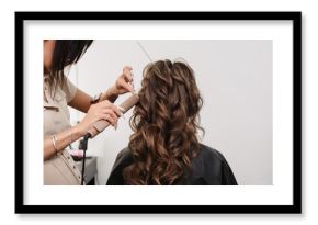 hairdresser makes a hairstyle for a girl bride with long curly brown hair