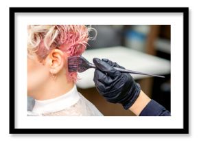 Hand of hairdresser dyeing hair in pink color by paintbrush on back of head of young caucasian woman in beauty salon