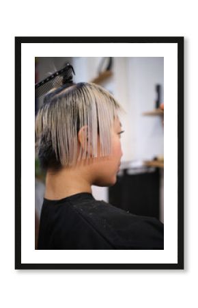 Hairdresser cutting wet hair of young female model in salon