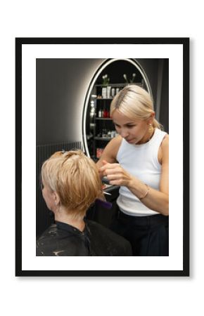 Female hairdresser styling blonde hair of caucasian adult woman in salon