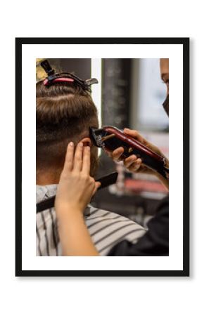 Vertical close-up photo of a hairdresser doing a machine haircut with a special attachment for a man. Barber cuts a man's temples. Hairdresser while working in a beauty salon, at barbershop