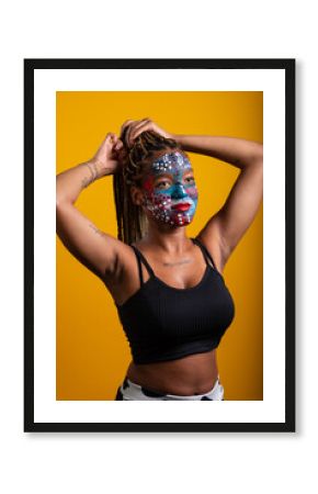 Young woman wearing black blouse holding braids in her hair with face painted with colorful paint, concentrated woman.