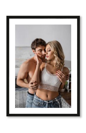 Sexy woman in bra touching muscular boyfriend in bedroom.