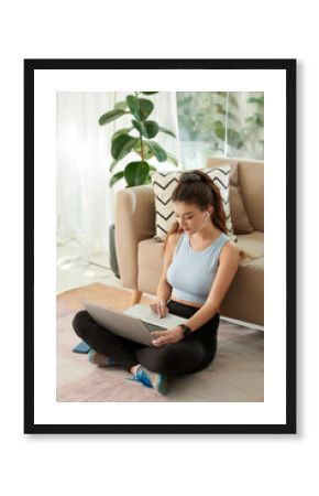 Young woman sitting on floor in living room and searching for online fitness class