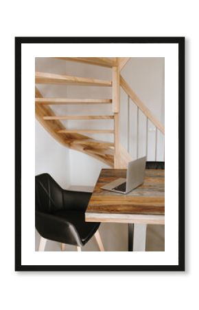 Home office desk workspace with laptop computer, solid wooden table, leather chair, staircase. Modern interior design concept