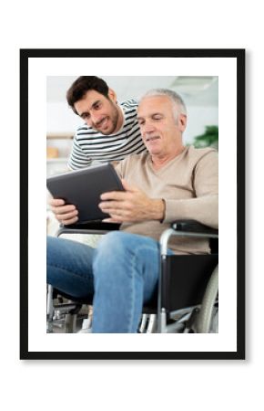 man showing digital tablet to his eldery father in wheelchair