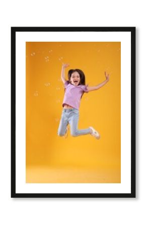 Little girl having fun with soap bubbles on yellow background