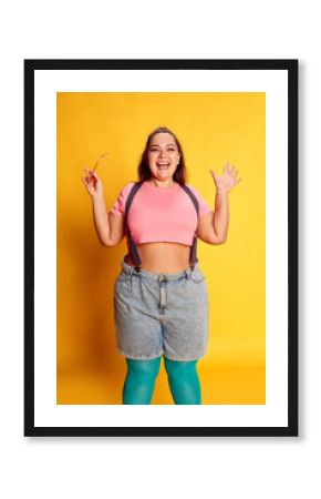 Super happy. Portrait of young overweight woman in casual bright clothes posing with smile over vivid yellow studio background