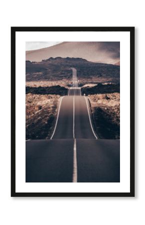 Endless road on a volcano in Timanfaya National Park in Lanzarote in the Canary Islands with a continuous line, black volcanic rocks on the side and volcanoes in mist in background.