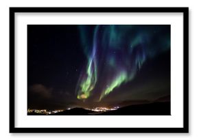 Glows of Northern Lights with shining stars on the sky over the mountains and highlighted city, Nuuk, Greenland