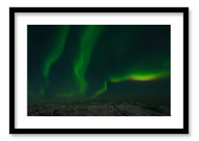 Northern lights, aurora in the night sky above the snowy hills.