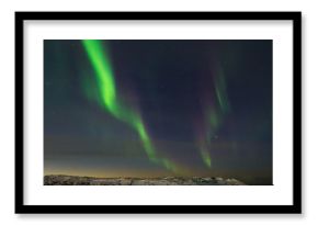 Beautiful northern lights, aurora in the night sky over the snow-covered hills.