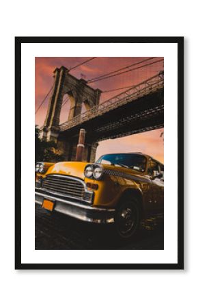 Vintage yellow taxi cab in New York under the Brooklyn Bridge with a colorful sky during sunset