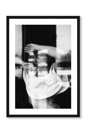 Black white photo portrait of beautiful woman in white dress posing near window