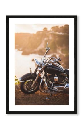 Old vintage motorcycle standing on the edge of cliff in warm sunlight at sunrise, shiny details of bike close-up