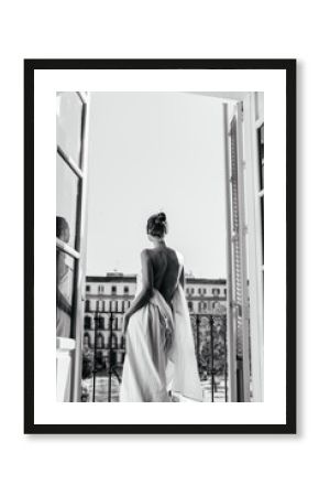 A girl resting at the hotel stands in the opening of an open balcony, wrapped in a sheet. The naked back is turned to the camera, photo black and white