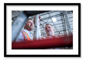 Businessman and man in reflective vest talking in industrial hall