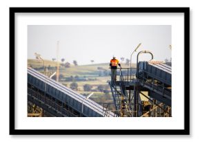 Worker wearing industrial safety vest with white helmet standing on a tall steel