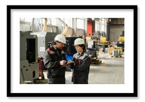 Workers in an industrial workshop engaging in discussion, dressed in protective work attire and helmets