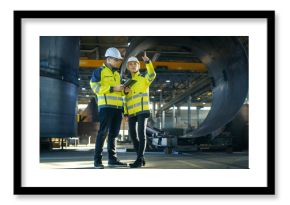 Male and Female Industrial Engineers in Hard Hats Discuss New Project while Using Tablet Computer. They're Making Calculated Engineering Decisions.