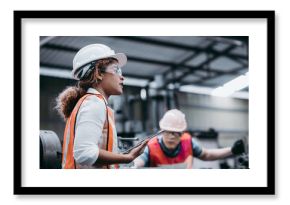 Female industrial engineer wearing a white helmet while standing in a heavy industrial factory behind she talking with workers, Various metal parts of the project
