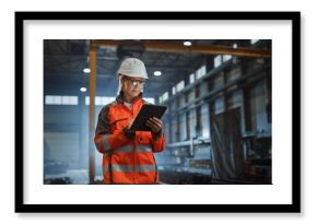 Professional Heavy Industry Engineer Worker Wearing Safety Uniform and Hard Hat, Using Tablet Computer. Serious Successful Female Industrial Specialist Walking in a Metal Manufacture Warehouse.