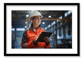 Professional Heavy Industry Engineer/Worker Wearing Safety Uniform and Hard Hat Uses Tablet Computer. Serious Successful Female Industrial Specialist Walking in a Metal Manufacture Warehouse.